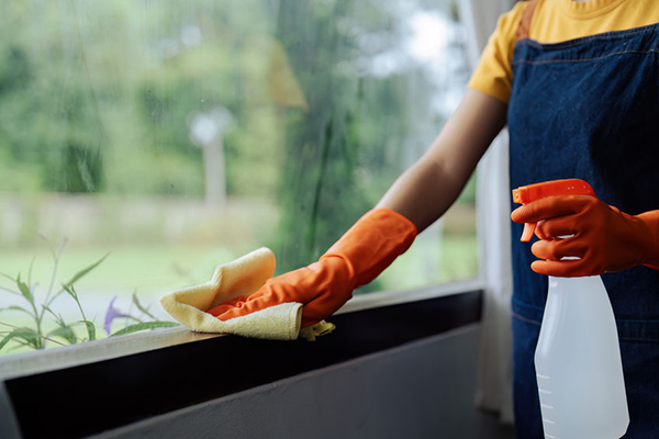 A female with orange gloves performing detailed cleaning on a windowsill